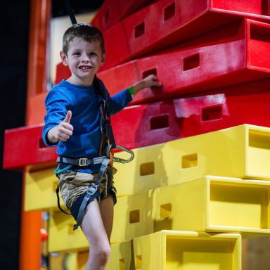 Little boy giving thumbs up while climbing in the Clip and Climb arena at High Rise Lisburn